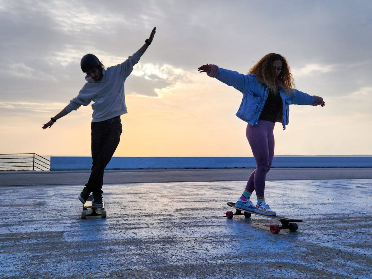 Two young adults skateboarding gracefully on a seaside promenade at sunset in İstanbul, Türkiye.