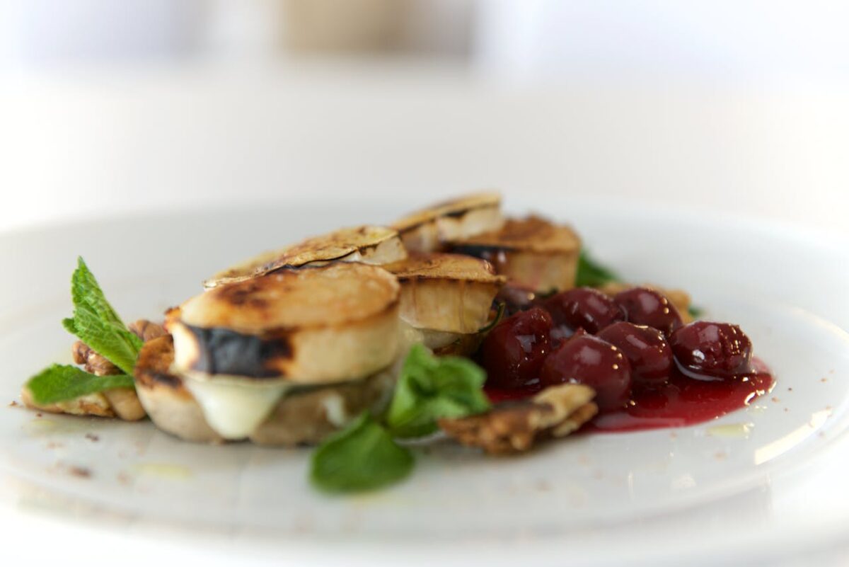 Elegant gourmet dish featuring toasted bread with melted cheese and cherry sauce, garnished with mint.