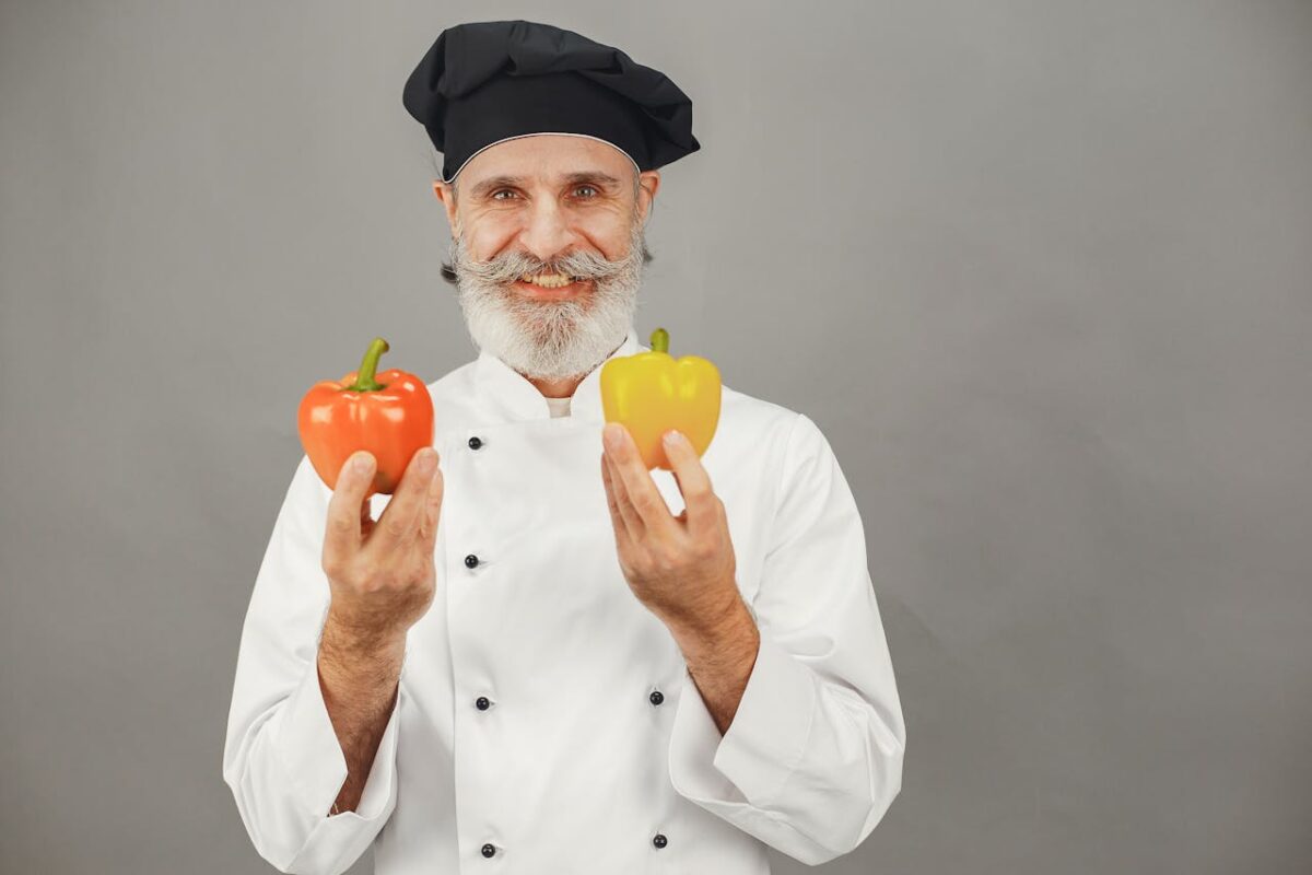Portrait of a smiling chef in uniform holding red and yellow bell peppers. Ideal for culinary and food-related themes.